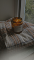 A candle placed on a blanket atop a window sill, softly illuminating the surrounding area.