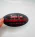 Black oval sticker with red gothic text reading “Zombie Love Kensington Paradise EXPERIENCE,” held against a white background.